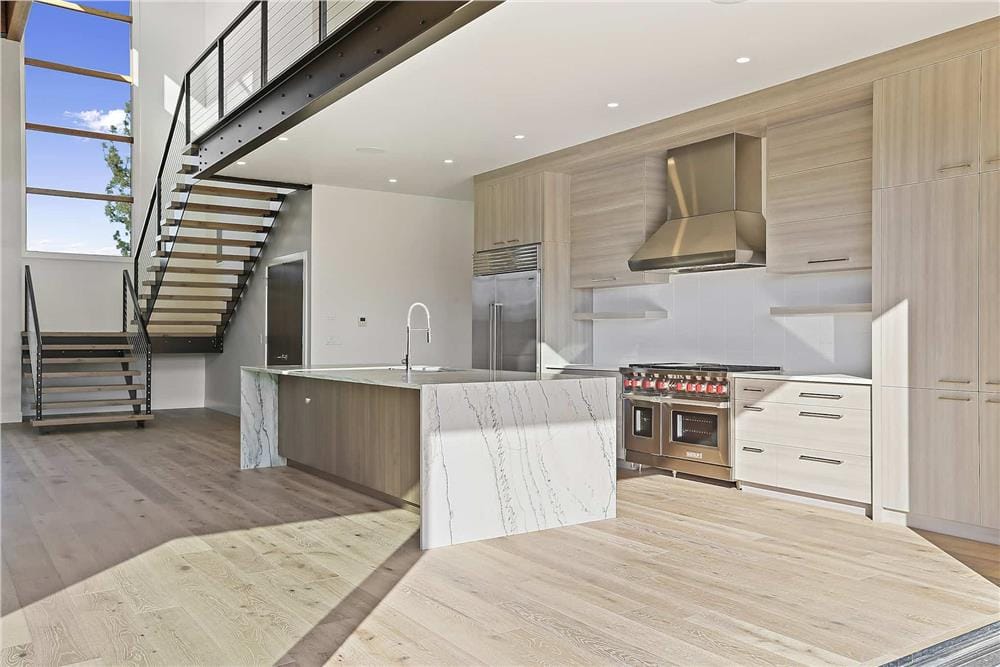 Kitchen with a waterfall island and light wood cabinets that blend in with the hardwood flooring.