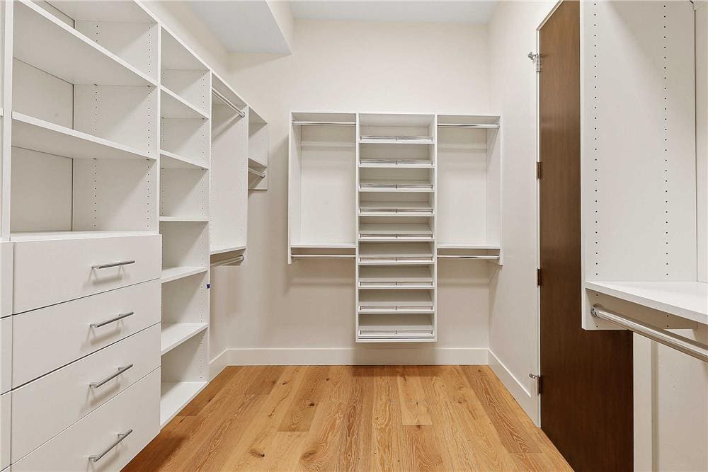 Primary walk-in closet with white built-ins and a hardwood floor.