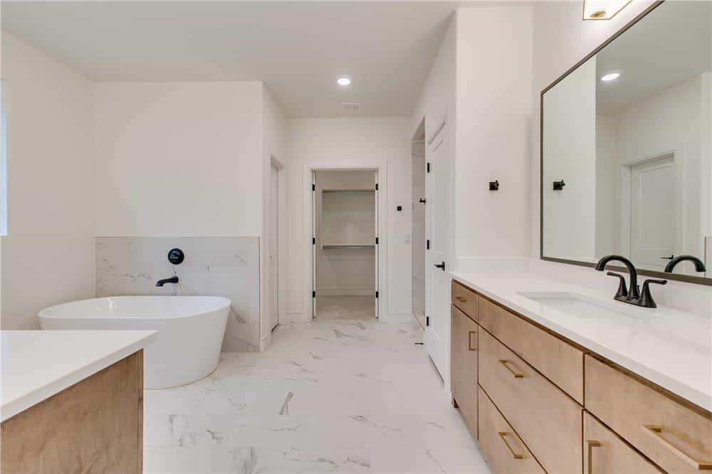 Primary bathroom with his and her sink vanities, a walk-in closet, and a soaking tub over marble-tiled flooring.
