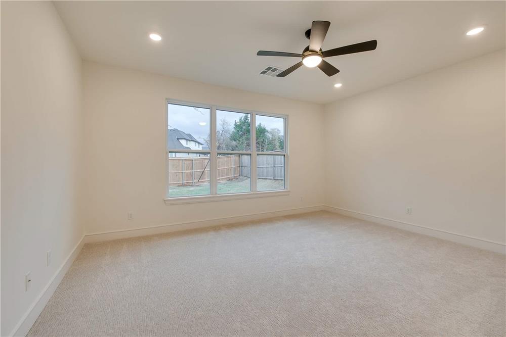 Primary bedroom with a carpeted floor and a trio of windows overlooking the backyard.