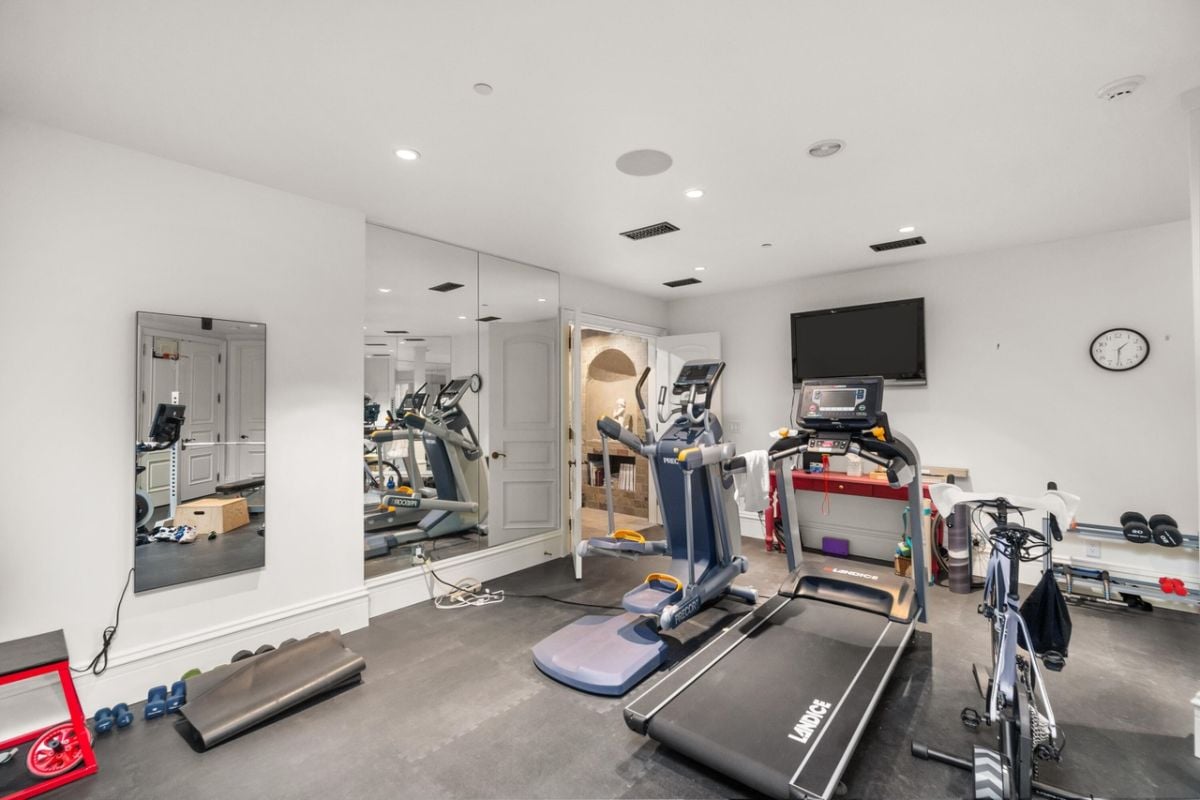 Home gym with workout equipment, TV and large mirrors.