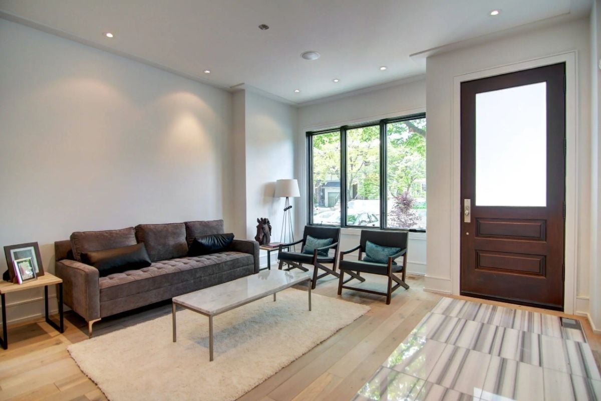 Living room with couches, wood flooring and large glass windows.
