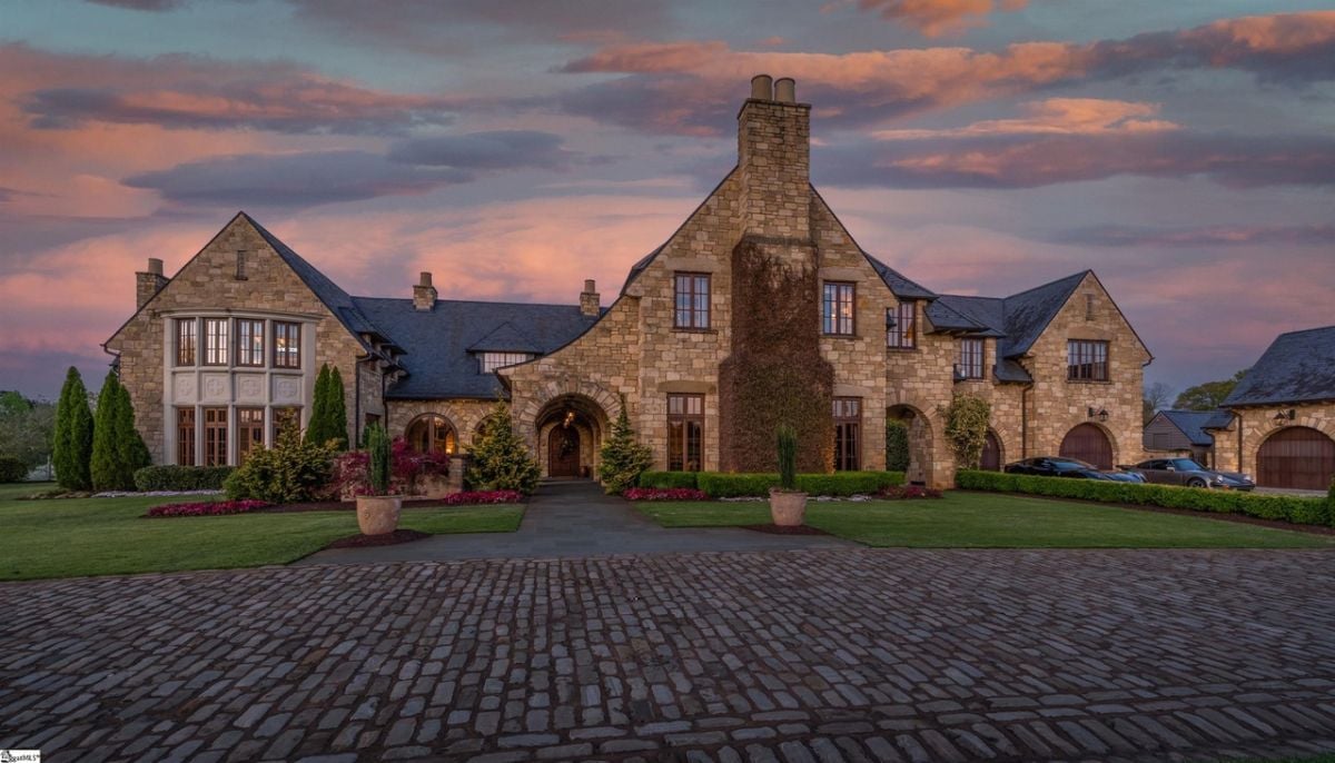 Front view of the mansion with a landscape and a huge driveway.