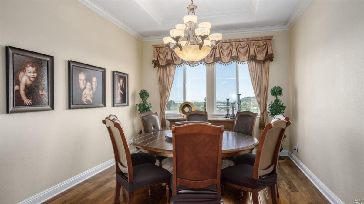Dining room with wood flooring, chandelier, wooden round table and chairs.