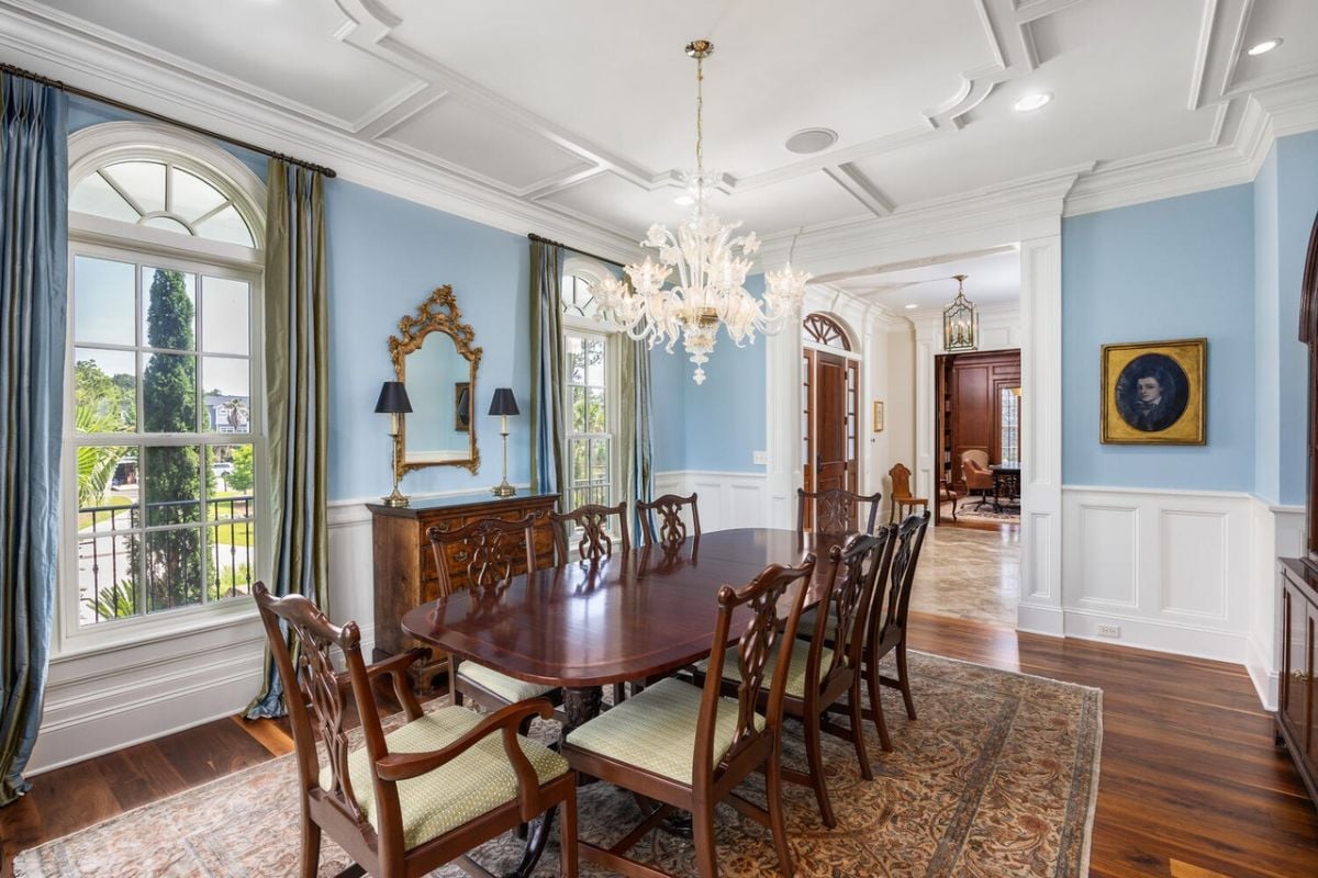 Dining room with a chandelier, a large wooden table and glass windows.