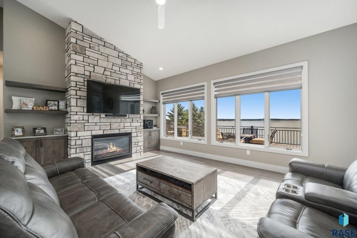 Living room with couches, a fireplace, a TV, glass windows and a view of the lake.