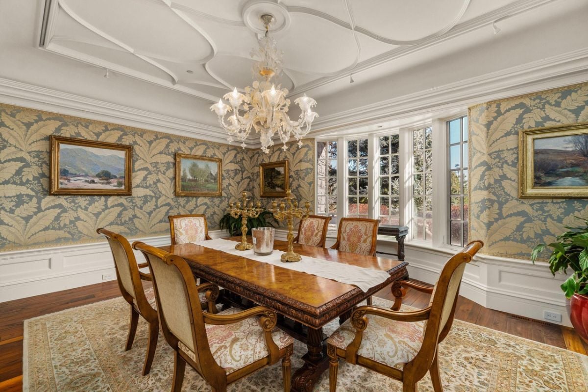 Dining room with a chandelier, glass windows, a large wooden table and chairs.