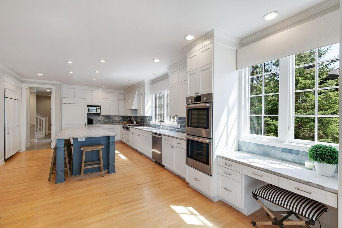 Kitchen with large glass windows, white cabinets, and a wooden floor.