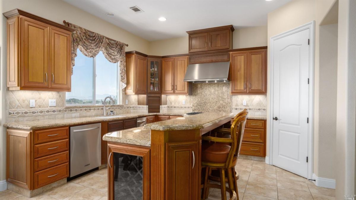 Kitchen with a sink, tile flooring, a large island, granite countertops, and custom cabinets.