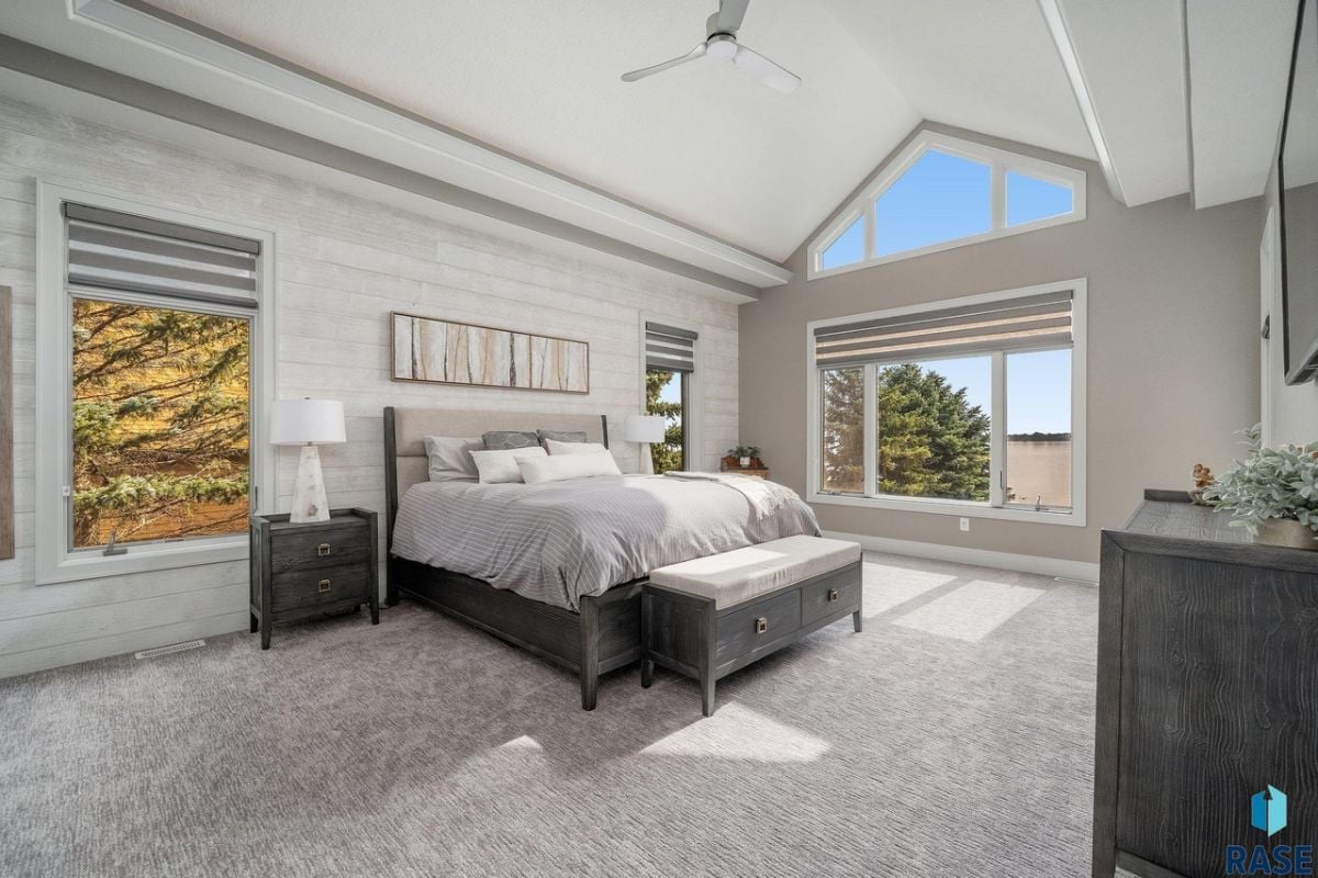 Bedroom with carpet flooring, a large bed and glass windows.