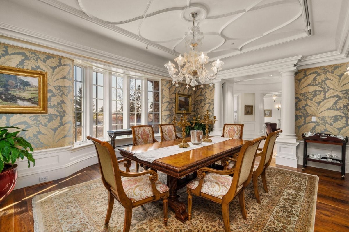 Dining room with a chandelier, glass windows, a large wooden table and chairs.