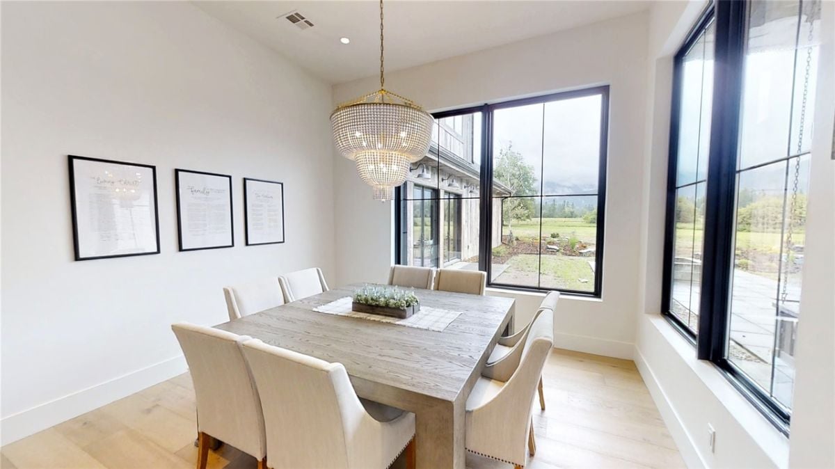Dining room with a chandelier, wooden table and large glass windows.