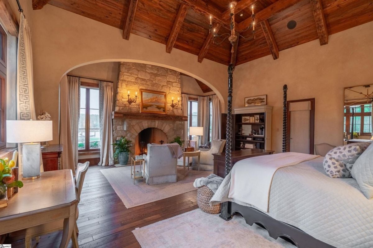 Bedroom with a fireplace, vaulted ceiling, wood flooring and glass windows.