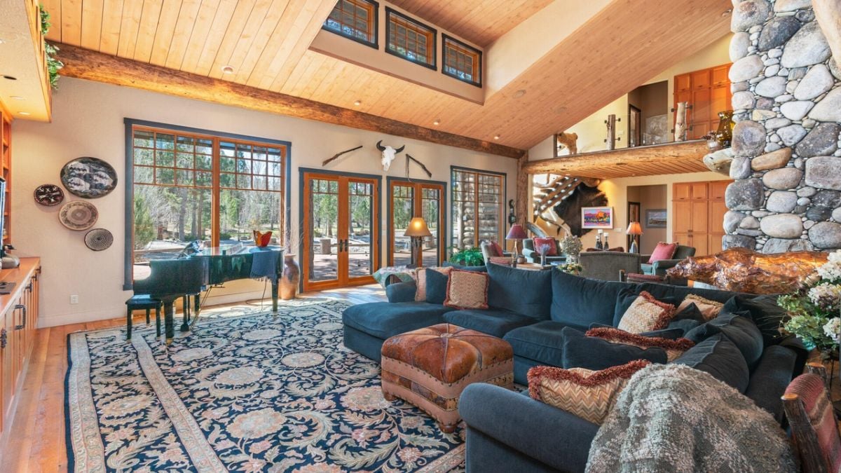 Living room with couches, piano, glass doors and glass windows.