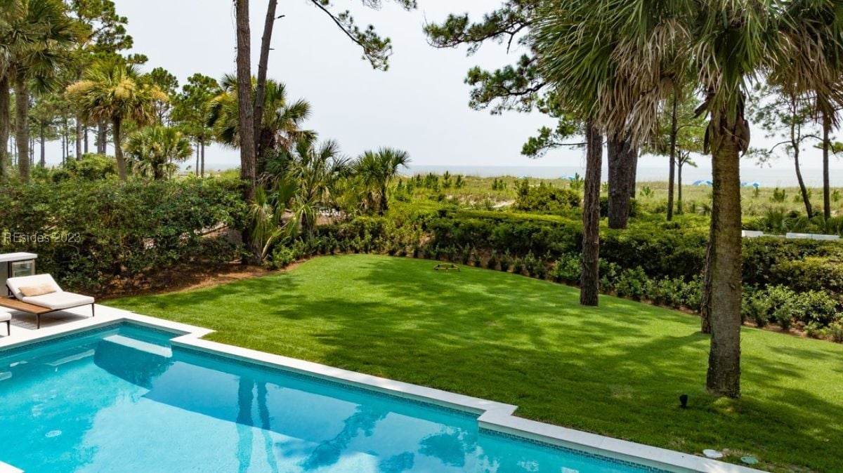 Pool with large green backyard lawn and a view of the ocean.