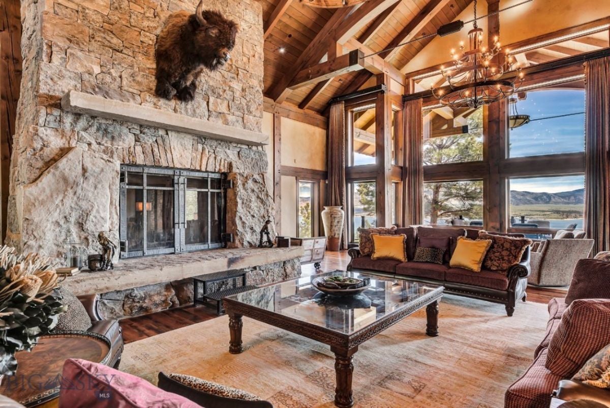 Living room with couches, chandelier and a large stone fireplace.
