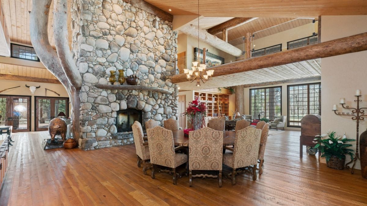 Dining room with round wooden table, chandelier, and a large stone fireplace