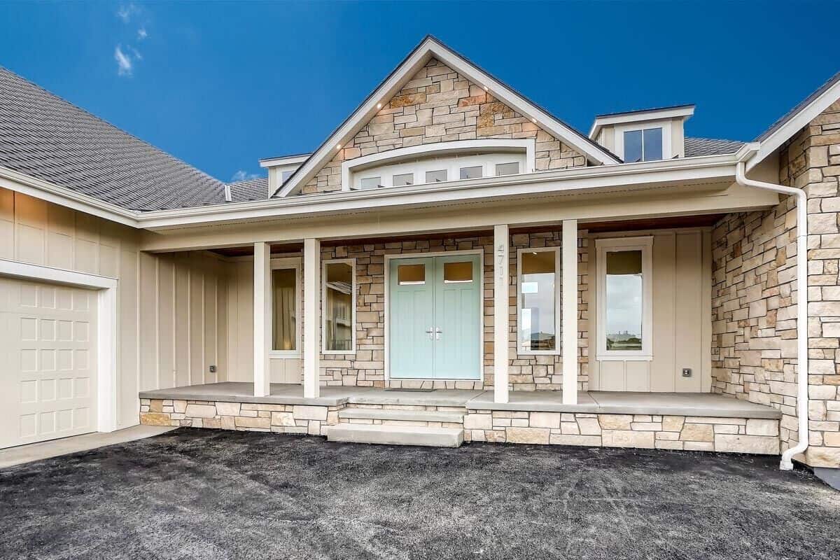 Front porch with a stone stoop, columns, and double entry doors topped with a center gable and dormer windows.