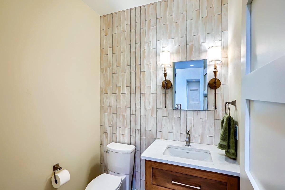Powder bath with a toilet and a sink vanity highlighted by linear mosaic tiles.