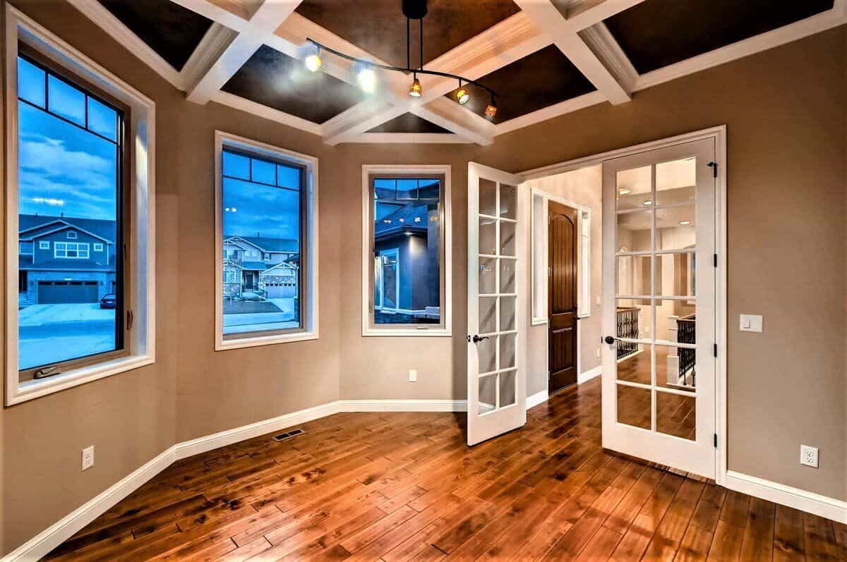 Home office with a French door, a coffered ceiling, and a bay window that looks out the front yard.