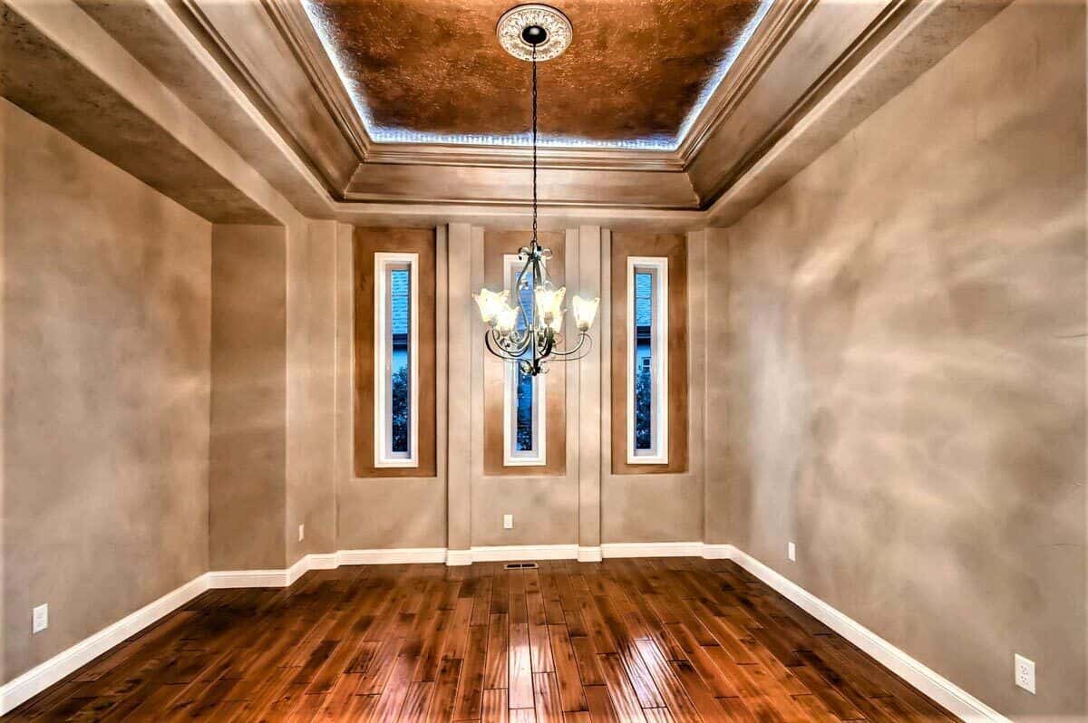 Dining room with slim windows and a decorative tray ceiling mounted with an ornate chandelier.