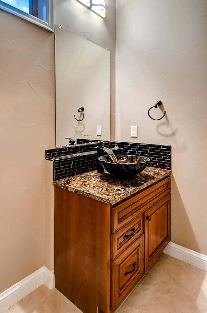 Powder bath with a vessel sink vanity topped with a frameless mirror.
