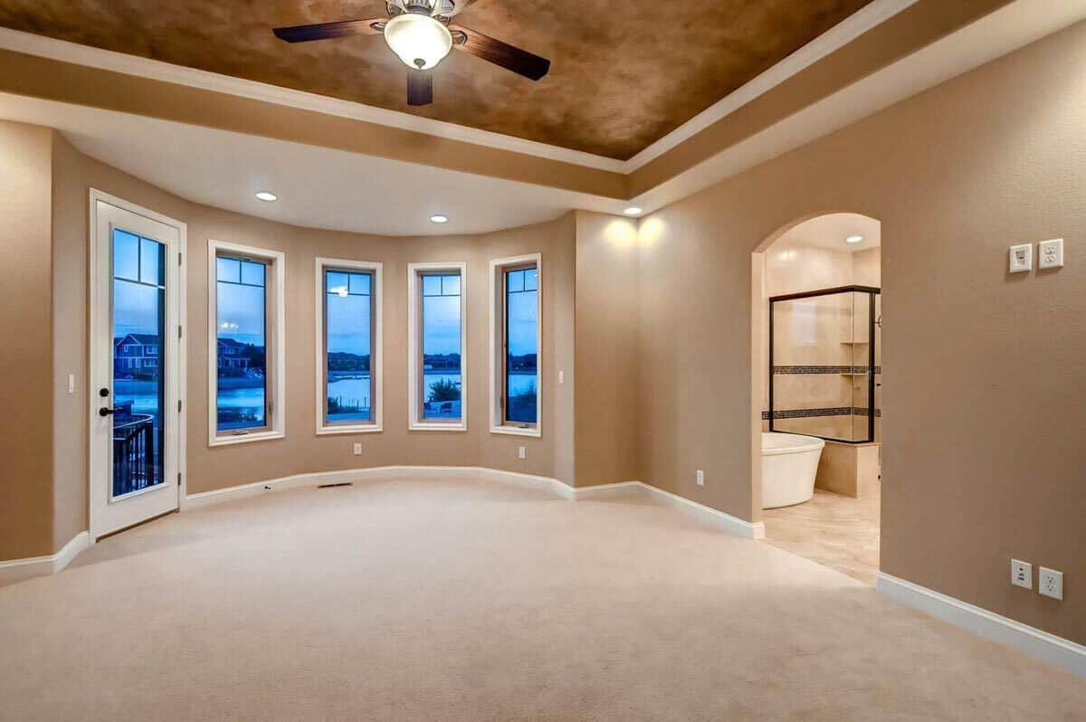Primary bedroom with a tray ceiling, a sitting area by the bow window and outdoor access through a glazed door.