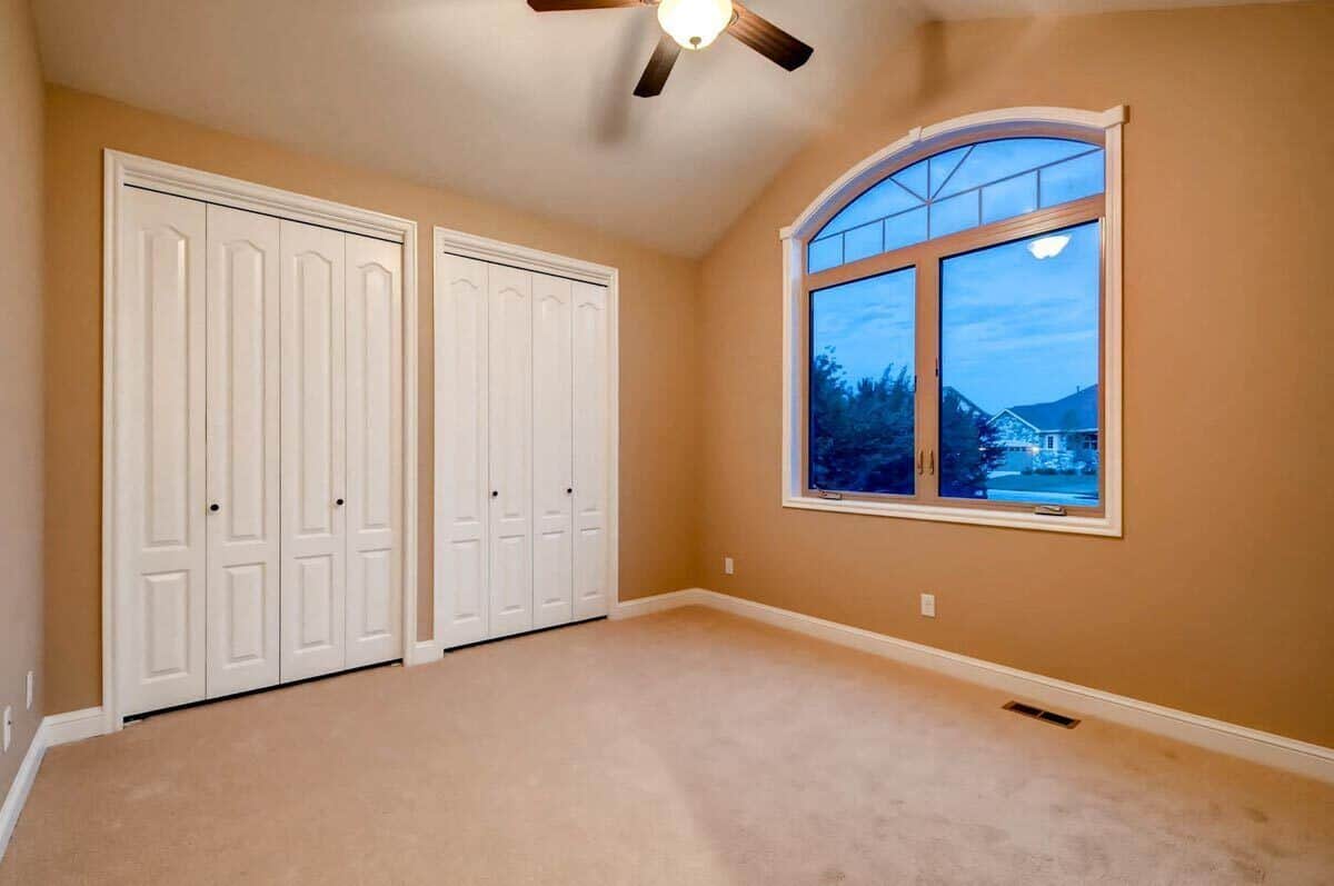 Secondary bedroom with a cathedral ceiling and built-in closets resting behind white double doors.