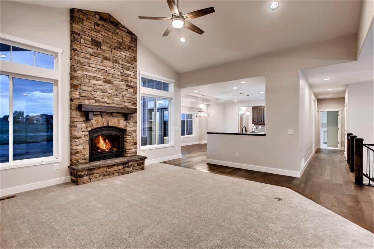 Great room with a cathedral ceiling, a carpeted floor, and a stone fireplace lined with a rustic mantel.