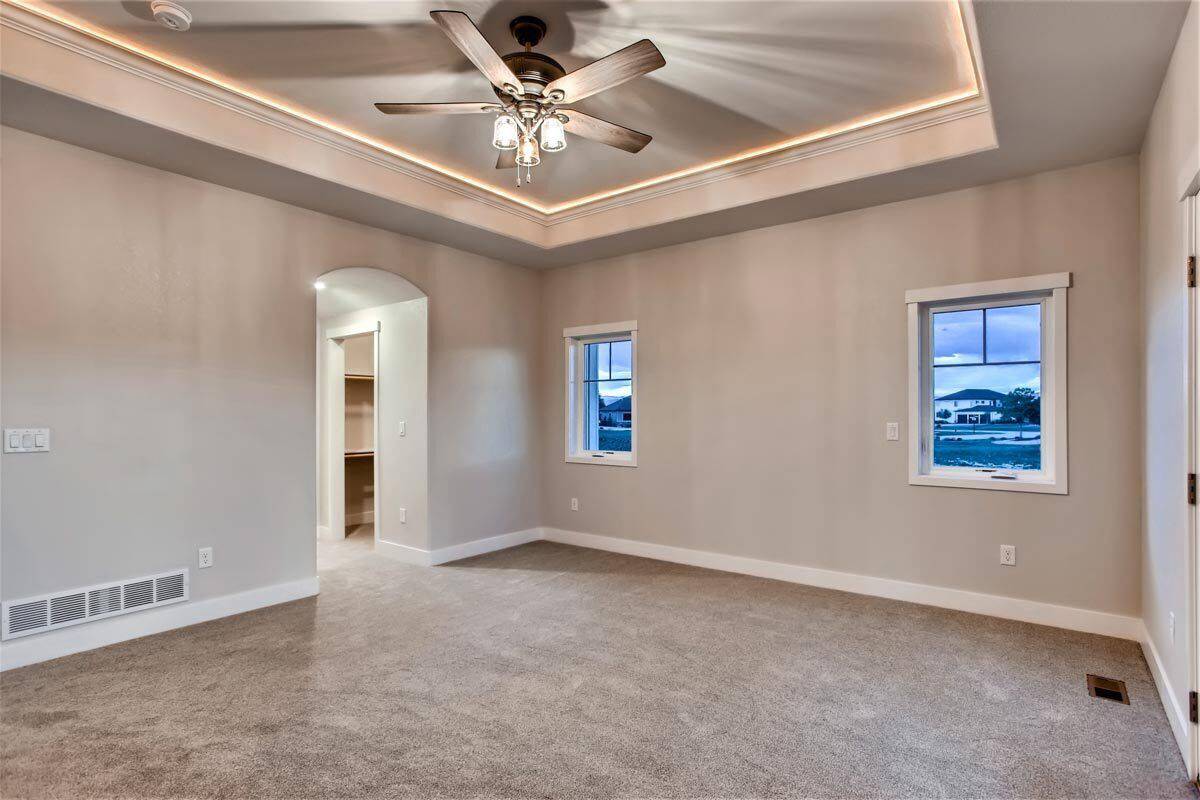 Primary bedroom with carpeted floor and a tray ceiling mounted with a traditional fan.