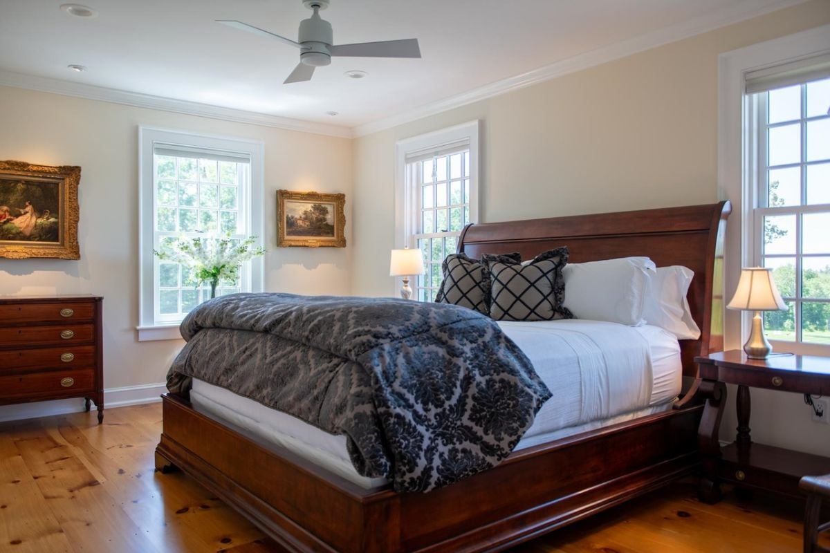 Bedroom with wood flooring, a ceiling fan, large bed, and glass windows.