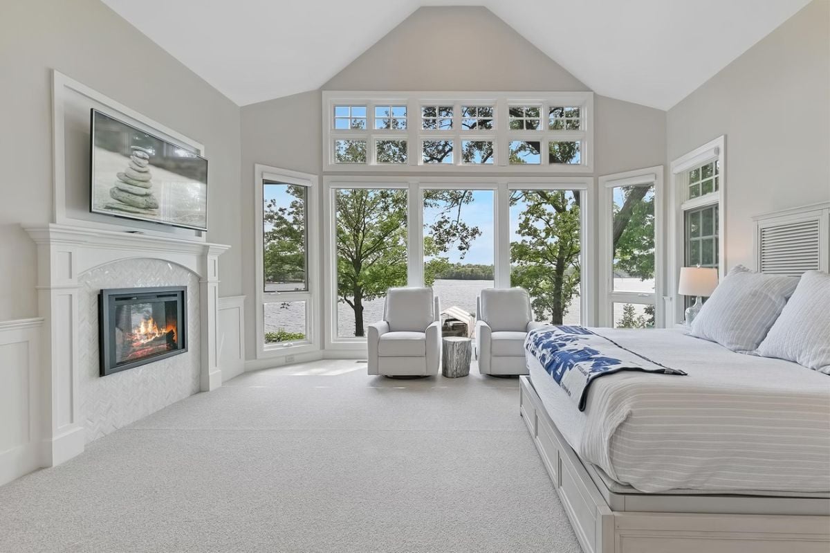 Bedroom with carpet flooring, fireplace and a view of the lake.