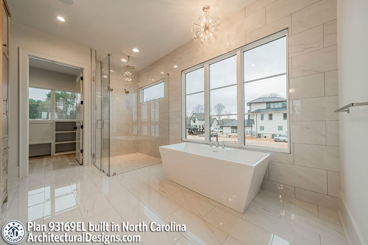 Primary bathroom with a walk-in closet, a tiled shower, and a soaking tub situated under the large windows.