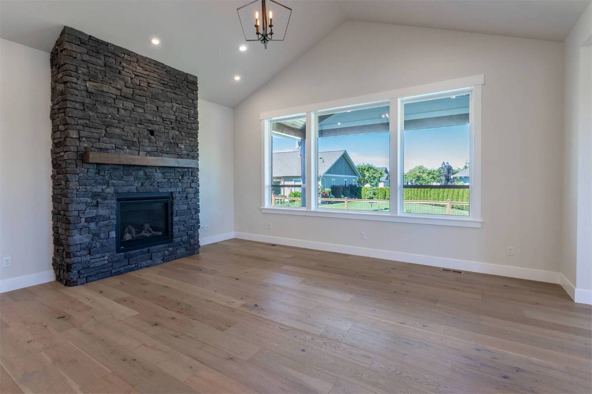 Great room with a stone fireplace, a cathedral ceiling, and a trio of windows overlooking the backyard and covered porch.