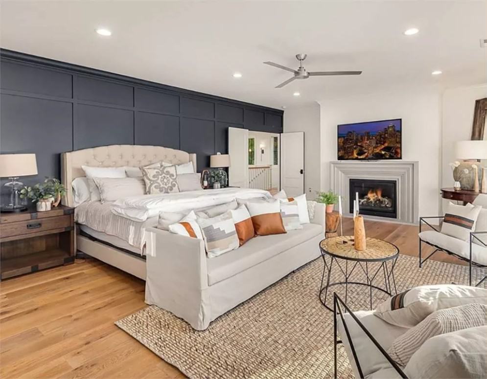 Primary bedroom with a paneled accent wall, a tufted bed, a fireplace, and a sitting area over the jute rug.