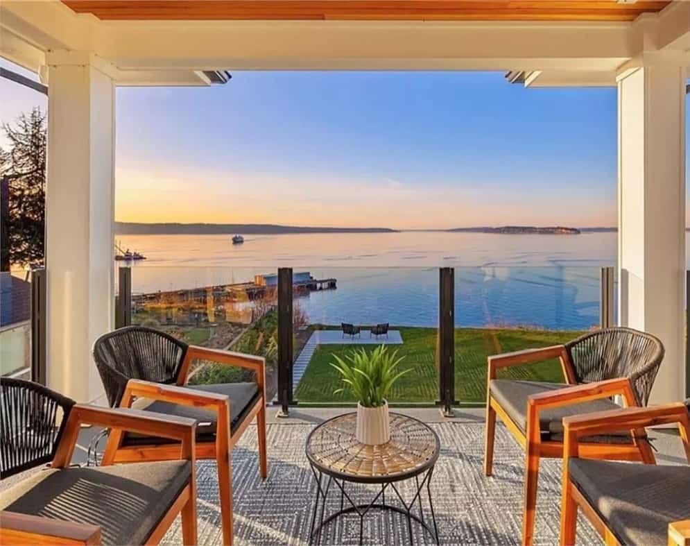Balcony with cushioned armchairs, a round table, and glass railings.