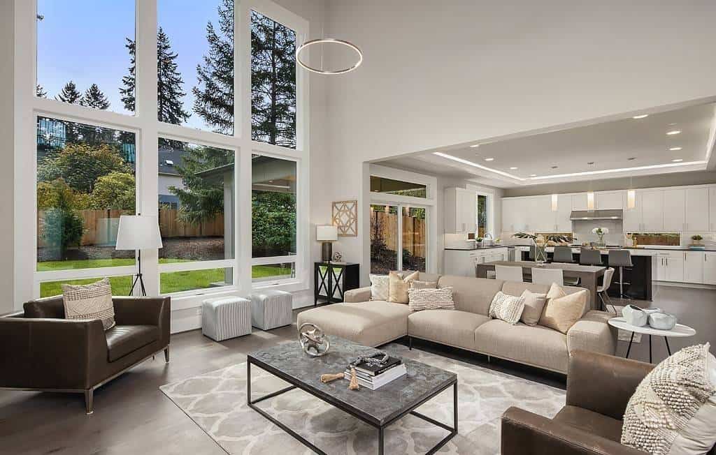 Family room with an L-shaped sofa, leather armchairs, and a wall of windows overlooking the backyard.