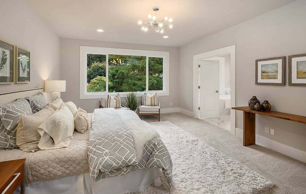 Primary bedroom with a carpeted floor, a wooden table, and a sitting area by the windows.