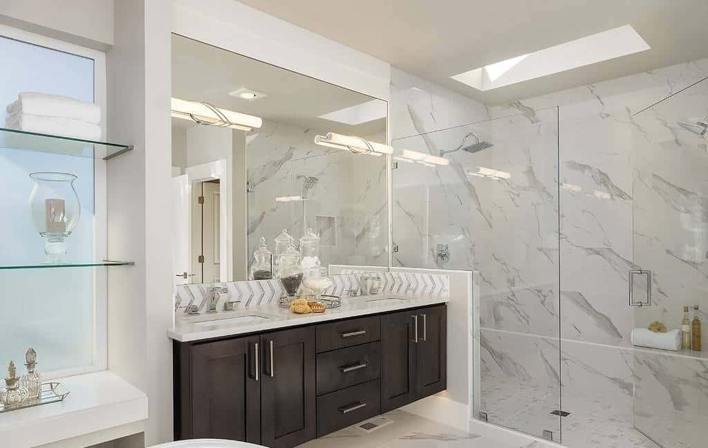 Primary bathroom with a dual sink vanity and a tiled shower illuminated by a skylight.