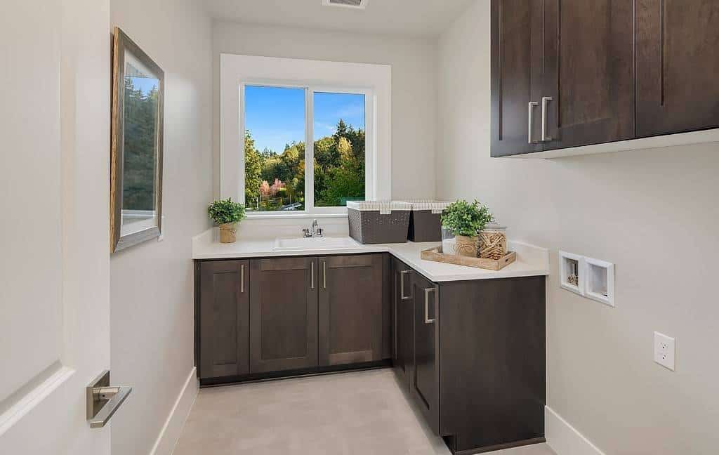 Laundry room with L-shaped counters, dark wood cabinets, and a sink with views of the lush greenery.