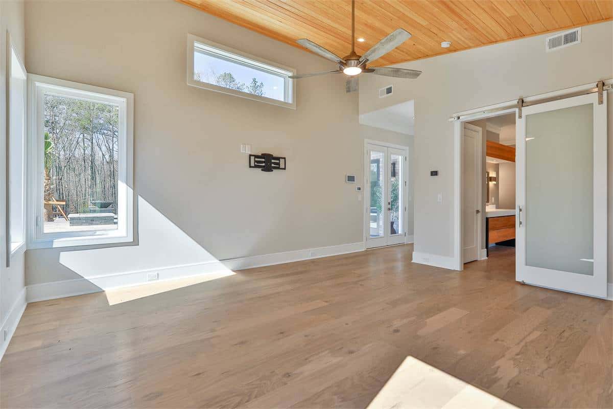 Primary bedroom with corner windows, a wood-paneled ceiling, and a sliding barn door that reveals the ensuite bath.
