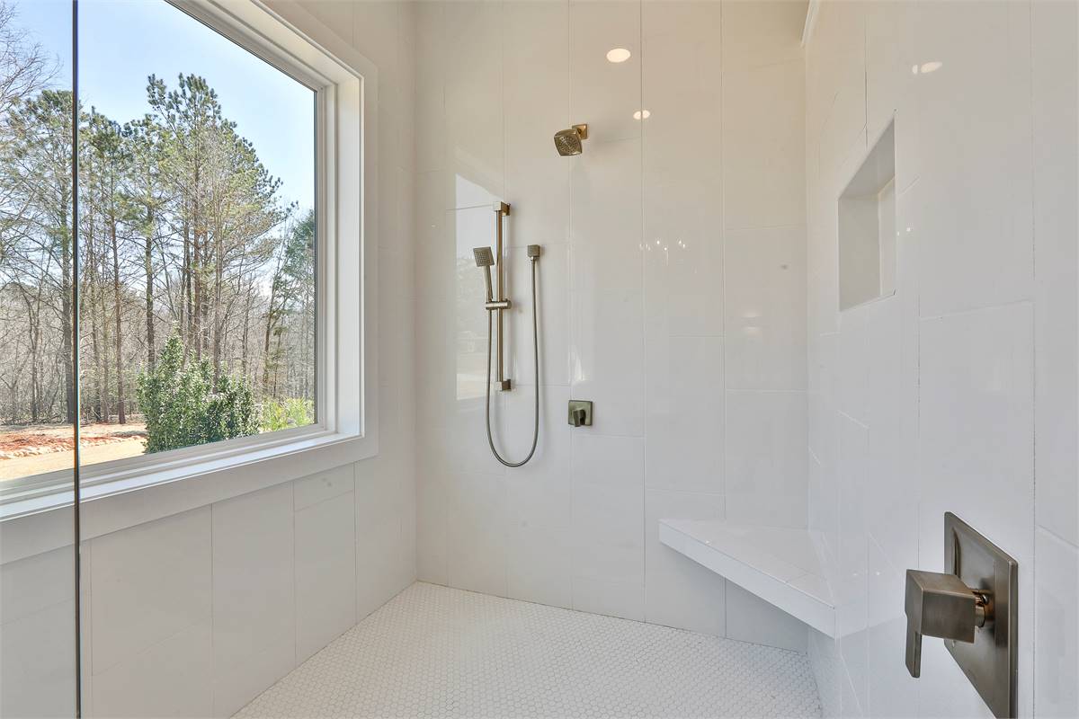Primary walk-in shower with chrome fixtures, a corner seat, and a large picture window that looks out the forest.