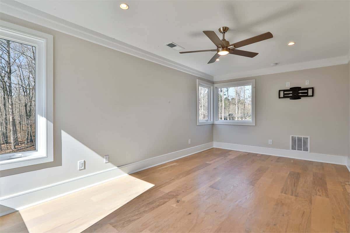 Secondary bedroom with large windows, light gray walls, and a hardwood floor.