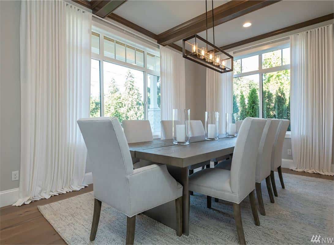 Dining room with a wooden dining set and a linear chandelier hanging from the beamed ceiling.