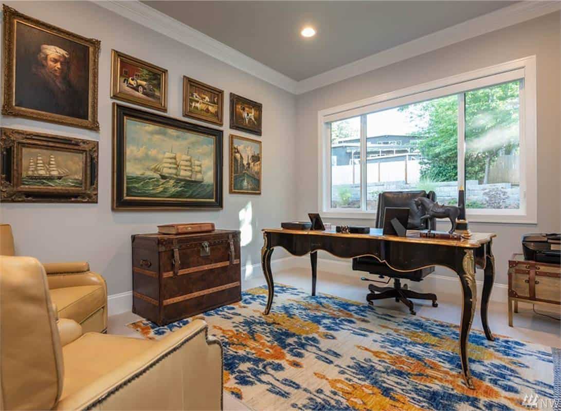 Home office with leather chairs, a dark wood desk, and gray walls adorned with framed paintings.