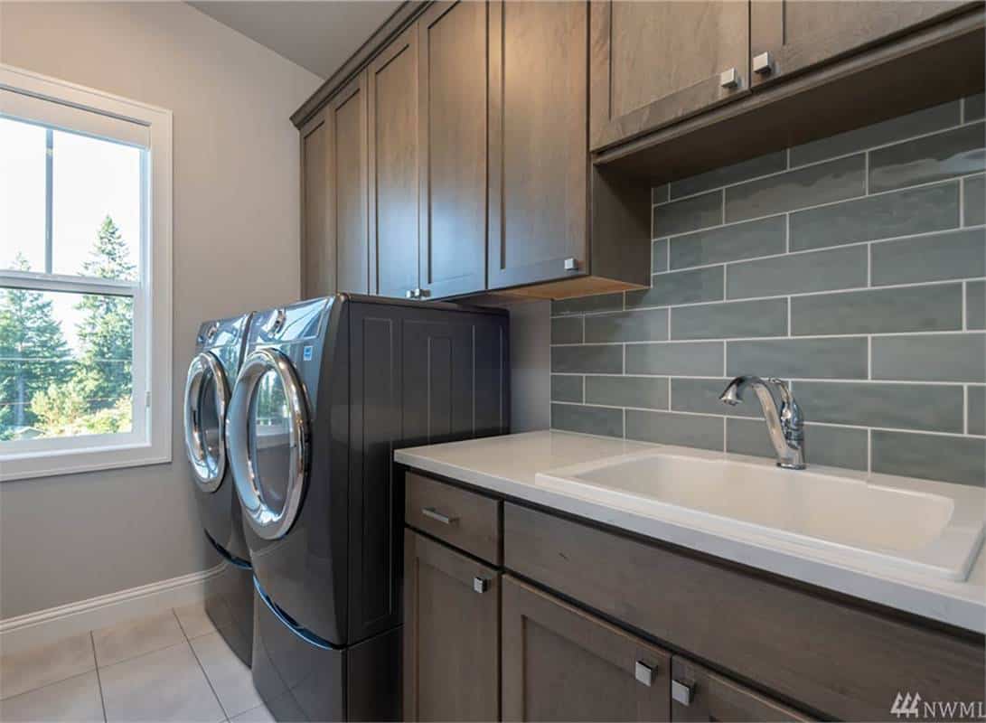 Laundry room with wooden cabinetry, a large sink, and laundry appliances.