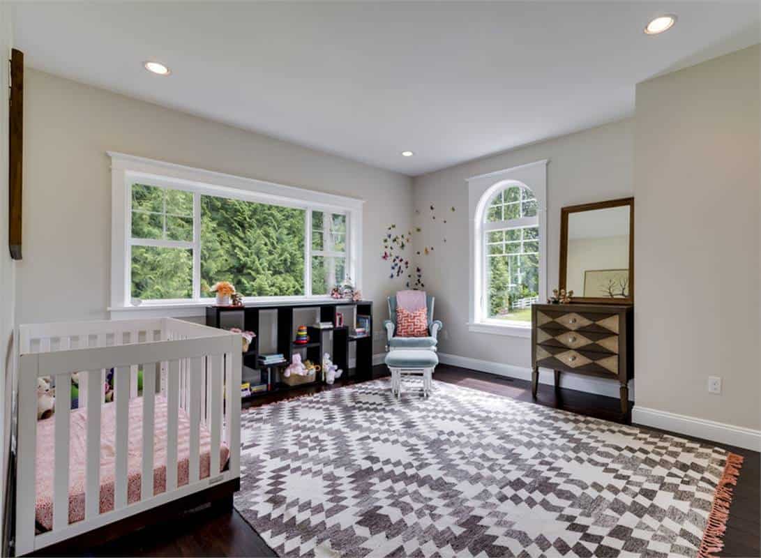 Nursery room with a white crib, dark wood cabinets, and a tasseled rug that lays on the hardwood flooring.