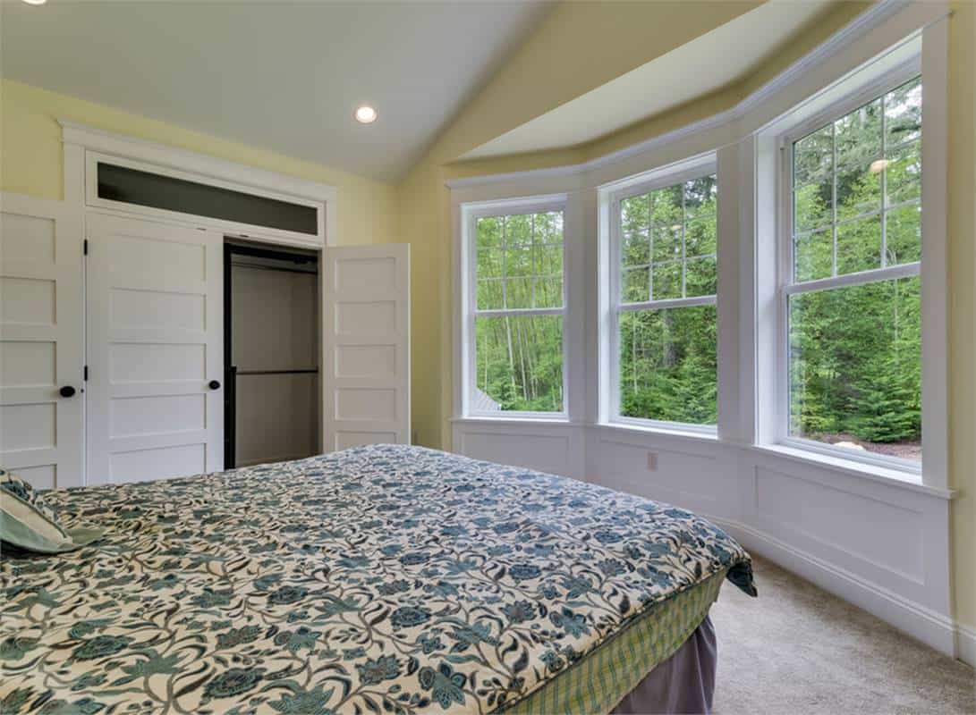 Secondary bedroom with a walk-in closet and a bay window that looks out the lush yard.