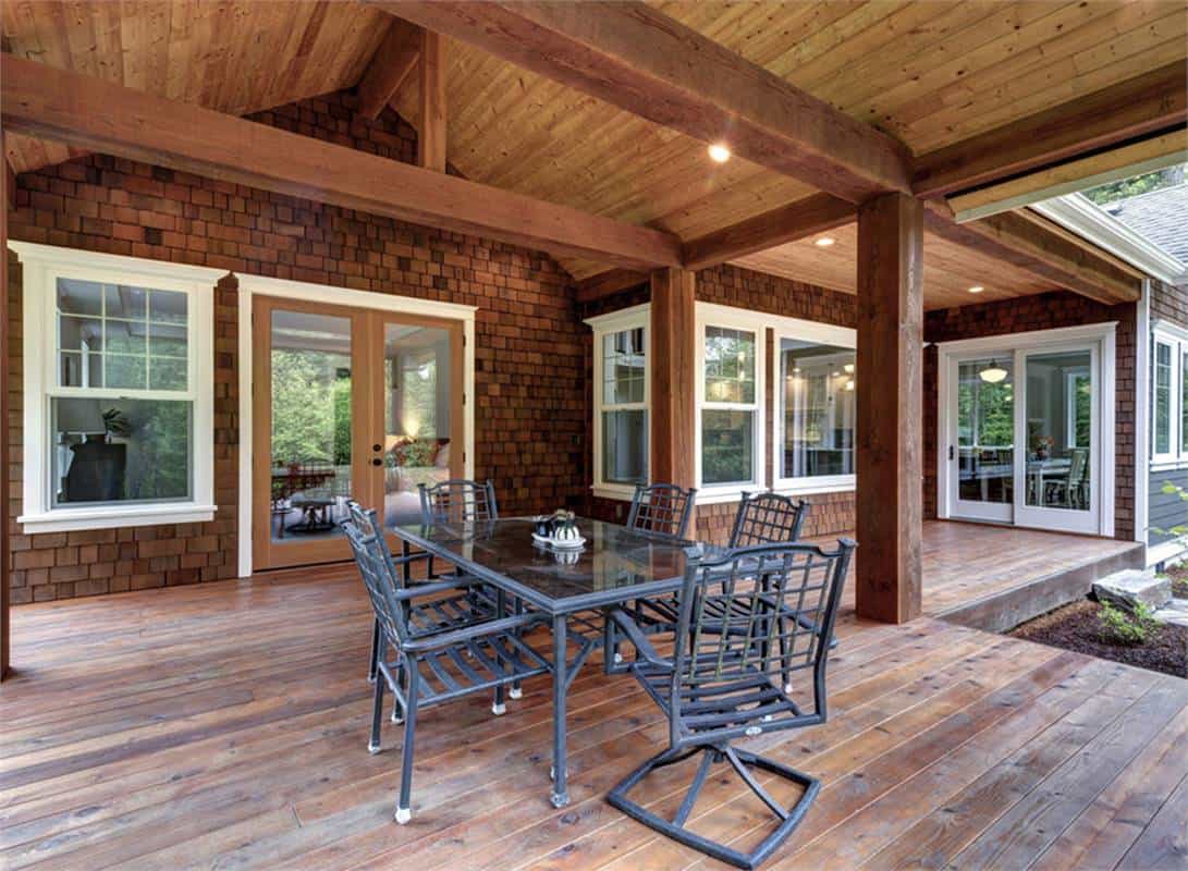 Covered rear deck with a metal dining set and a cathedral ceiling framed with exposed beams.