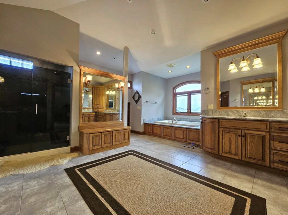 Bathroom with tile flooring, a rug, sinks and soaking tub.